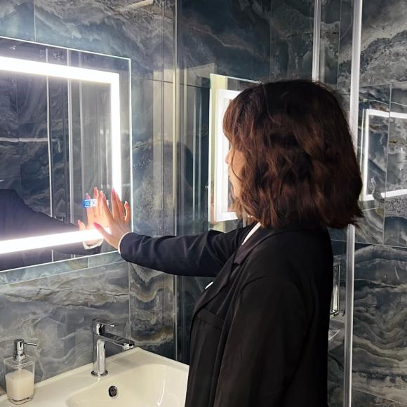 Woman touches a lit mirror in a stylish bathroom, reflective atmosphere.