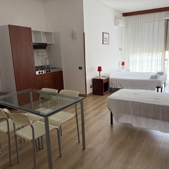Bright room with single beds, kitchenette, glass table, cozy atmosphere.