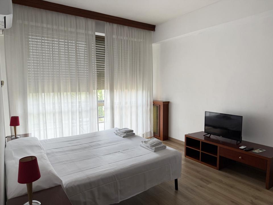 Bright room with white bed, sheer curtains, and TV on wooden stand.
